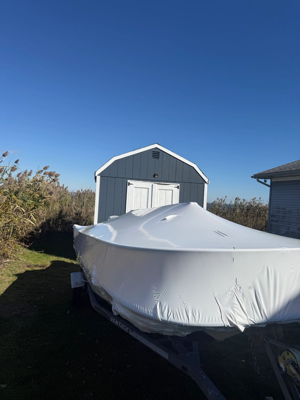 Boat covered with a white tarp beside a blue shed