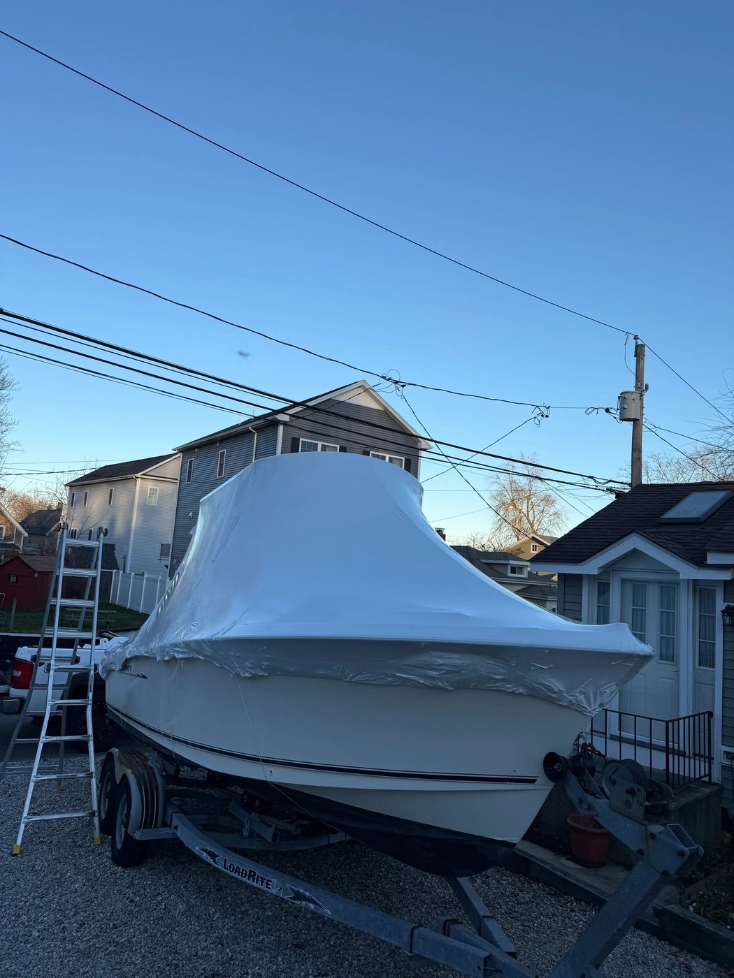 Boat wrapped in a protective white cover on a trailer in a residential area