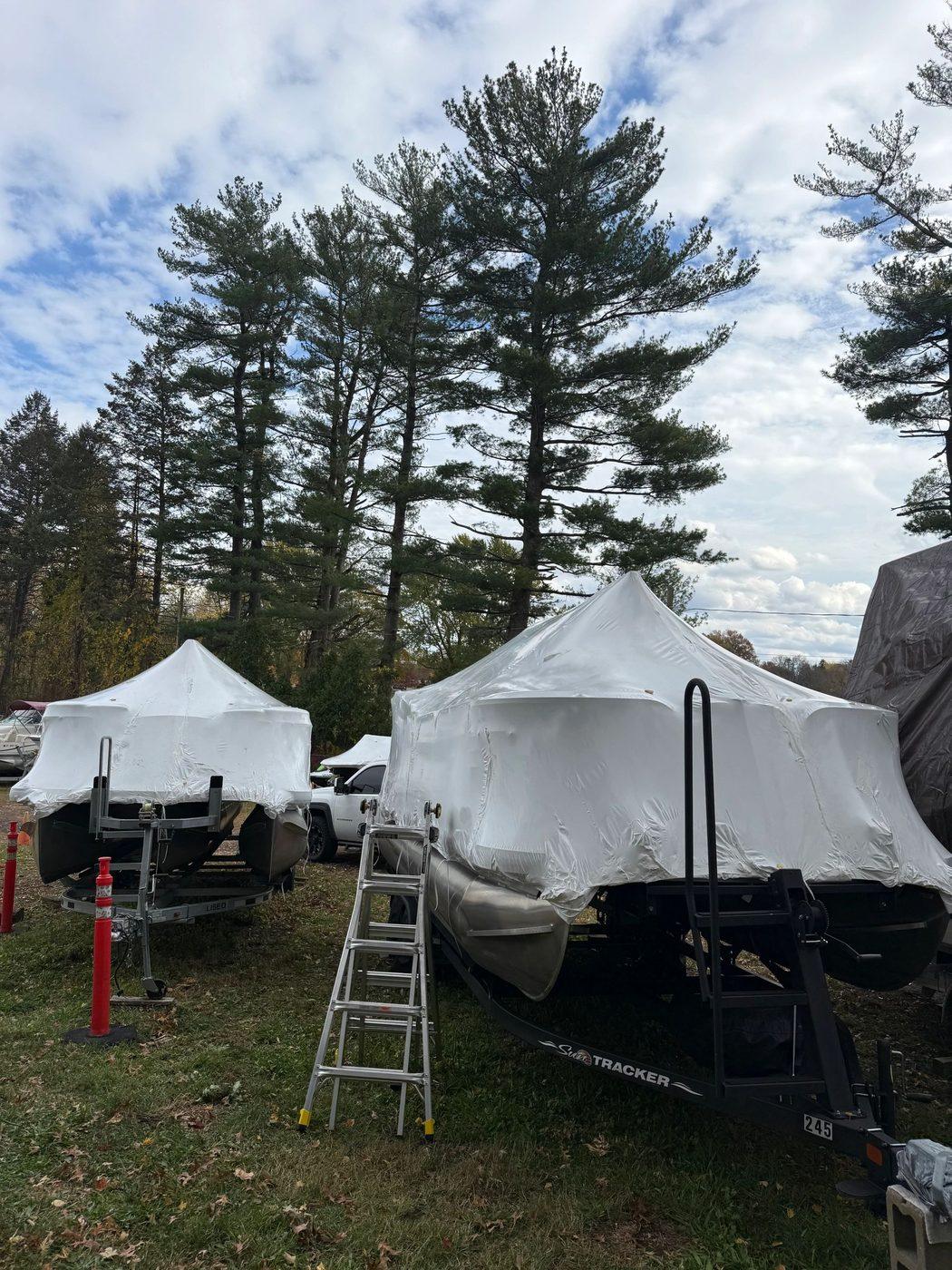 Two shrink wrapped boats parked on trailers in a wooded lot